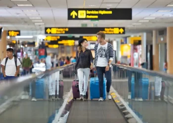 Pareja de jóvenes con maletas caminando por una pasarela en un aeropuerto