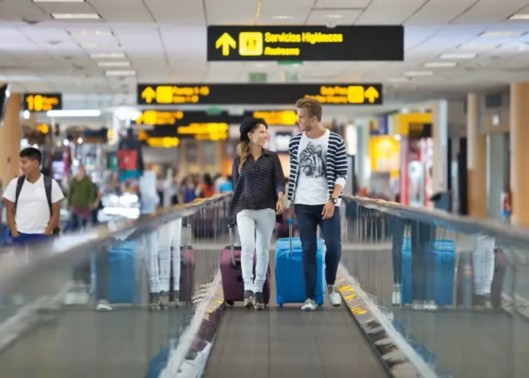 Pareja de jóvenes con maletas caminando por una pasarela en un aeropuerto